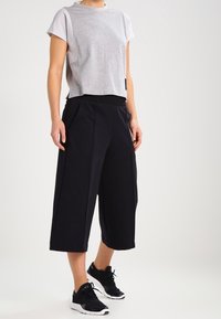 Szara krótka koszulka z krótkim rękawem zestawiona z luźnymi czarnymi kulotami i czarnymi trampkami. Swobodny, sportowy wygląd, gładkie faktury.