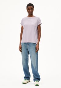 T-shirt di un leggero lavanda con maniche arrotolate, abbinata a jeans blu a vita alta. Il modello indossa scarpe da ginnastica color crema e verde.