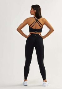 Crop top de sport noir avec des bretelles croisées, associé à un legging noir taille haute. Les deux ont une texture lisse et des logos minimalistes.