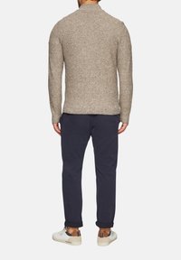 Beige gestrickter Pullover mit hohem Kragen, gerippten Bündchen und Saum. Kombiniert mit navyfarbenen Hosen und weißen Sneakers, was einen lässigen Lagenlook zeigt.