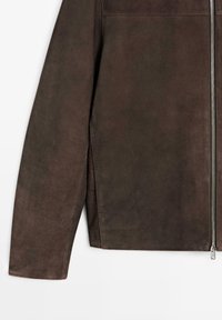 Manica e fianco di una giacca in suede marrone con cerniera argento visibile e spacco sulla cucitura laterale su sfondo bianco.