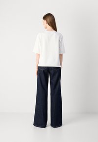 Hvit kortermet topp med rund hals, i kombinasjon med mørkeblå vidjeans med klassisk fem-lommers design og lys søm.
