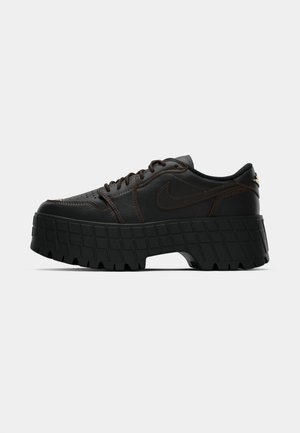 Sneaker Nike in pelle nera con suola piatta spessa e testurizzata e cuciture marroni su uno sfondo bianco semplice.