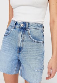 Jasnoniebieskie krótkie spodenki dżinsowe z wysokim stanem, efektami przetarć, postrzępionym wykończeniem i klasycznym wzorem z pięcioma kieszeniami. Teksturowana tkanina.