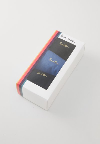 Tre paia di calzini in blu navy e nero, confezionati in una scatola bianca con una fascia a righe multicolori e testo dorato che presenta il nome del marchio.