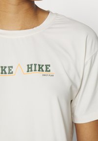Bílý krátký rukáv tričko vyrobené z měkké tkaniny s potiskem "HIKE" a "ONLY PLAY" v zeleném a oranžovém písmu, s kulatým výstřihem.
