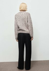 Un pull gris clair et duveteux avec un motif moucheté, associé à un pantalon large noir. Le pull présente un col rond et un ourlet côtelé.