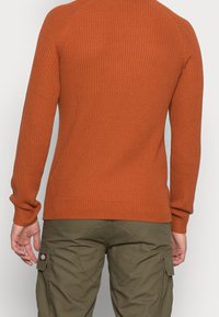 Sweter z prążkowanego dzianiny w kolorze spalonym pomarańczowym, z długimi rękawami i dopasowanym krojem. Miękka faktura z okrągłym dekoltem i wykończeniem na dole.