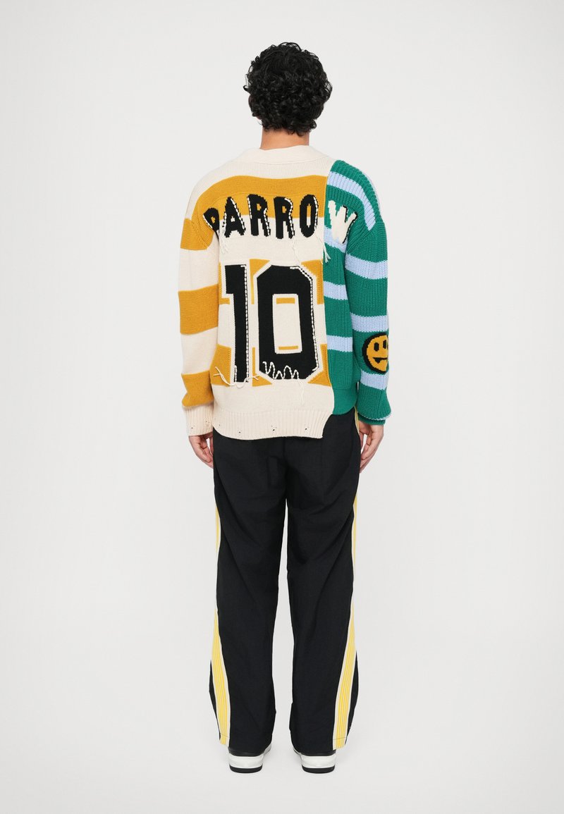 Pull en tricot avec un design multicolore : rayures beige, vertes et jaunes, grands chiffres noirs "10" et le texte "PARROW" au dos. Pantalons larges noirs en dessous.