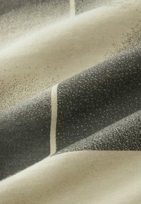 Gros plan d'un tissu montrant un motif texturé noir et beige avec de petits points éparpillés et une seule fine ligne verticale.