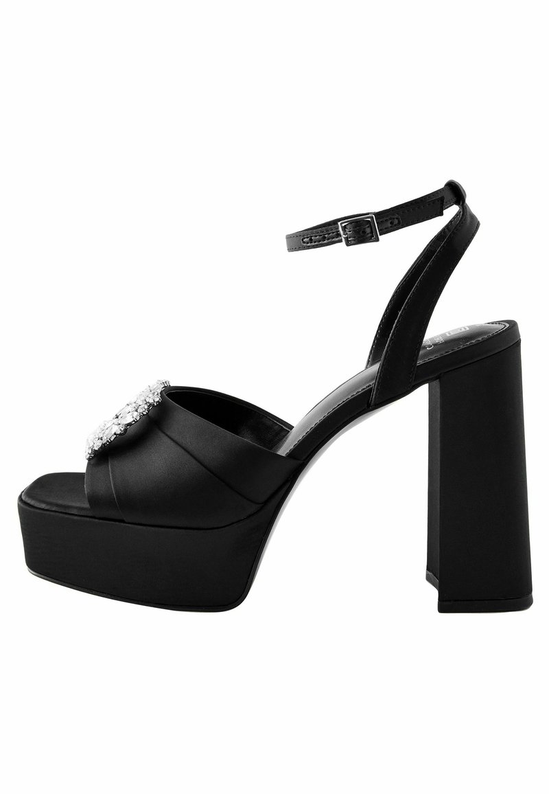 Black satin platform heels feature a wide block heel, open toe, ankle strap, and a decorative rhinestone accent on the upper.