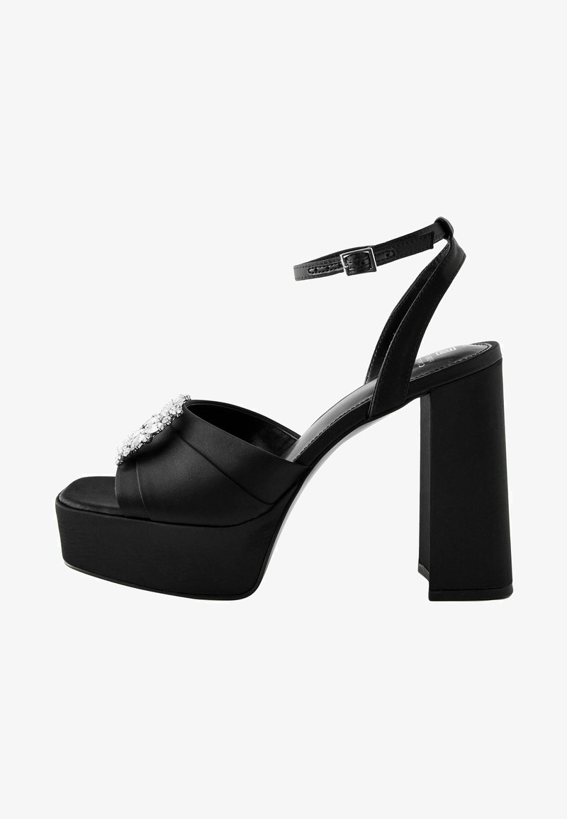 Black satin platform heels feature a wide block heel, open toe, ankle strap, and a decorative rhinestone accent on the upper.