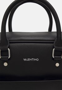 Crna torbica s teksturiranim završetkom, s nekoliko srebrnih dijelova. Na prednjoj strani nalazi se logo "VALENTINO". Dvostruki ručici za nošenje.