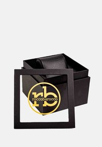 Must musta karp, millel on kaas ja millel on läbipaistvas ruudukujulises lõikepinnas kuldne logo. Sile tekstuur, minimalistlik stiil.