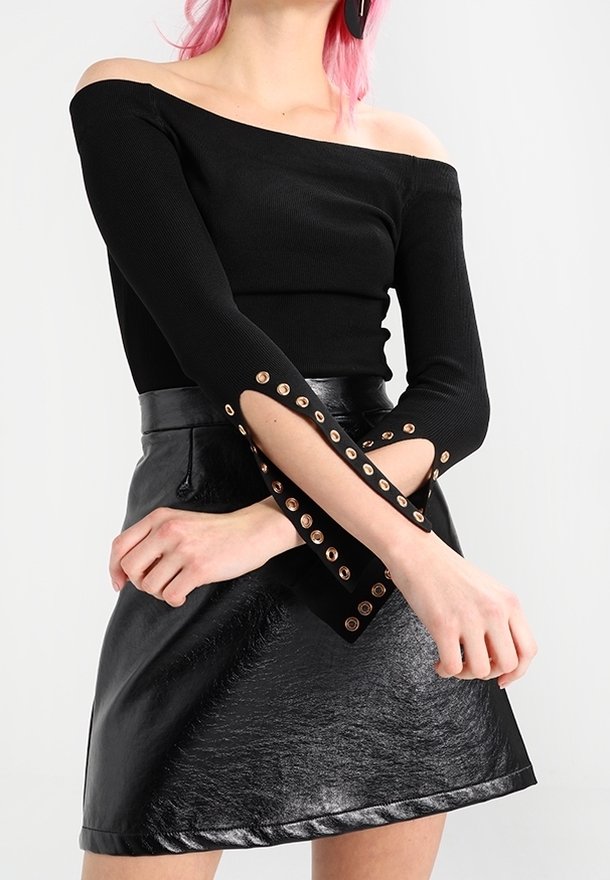 Black ribbed off-the-shoulder top with long sleeves featuring gold grommet accents and a fitted silhouette, paired with a shiny black skirt.
