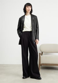 Blazer in pelle nera su una maglietta bianca, abbinato a pantaloni neri a vita alta e gamba larga e scarpe nere. Design minimalista e linee pulite.