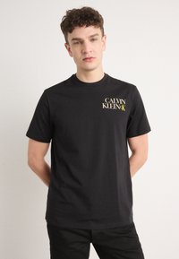 Sort bomulds t-shirt med korte ærmer, der har et frontlogo i guldtekst. Klassisk crew neck design med en lige kant.