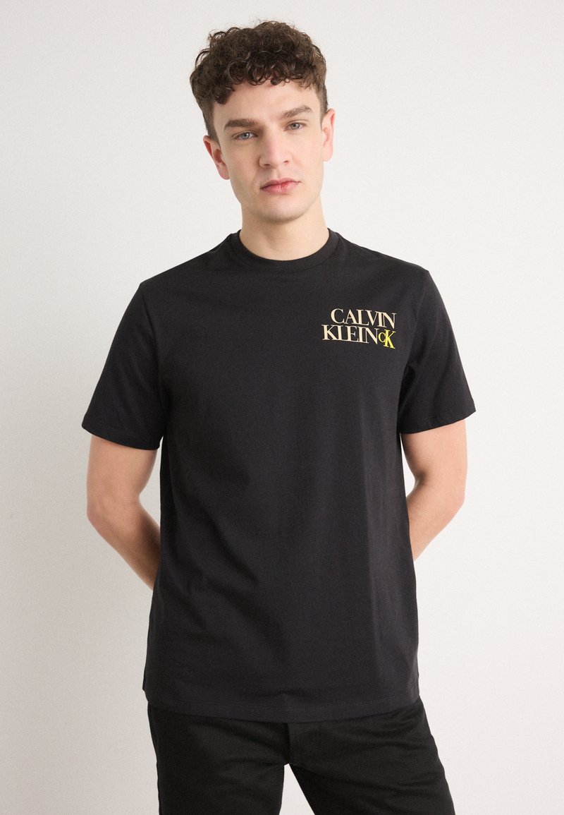 Sort bomulds t-shirt med korte ærmer, der har et frontlogo i guldtekst. Klassisk crew neck design med en lige kant.