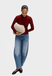 Rød tekstureret langærmet top, løstsiddende lyseblå denimjeans, sorte flade sko og en beige plisseret clutch taske. Fokus på enkel og afslappet stil.