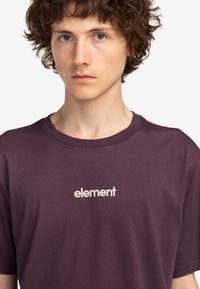 Camiseta de algodón morada con cuello redondo y mangas cortas, con la palabra "elemento" estampada en un tono claro en el pecho.