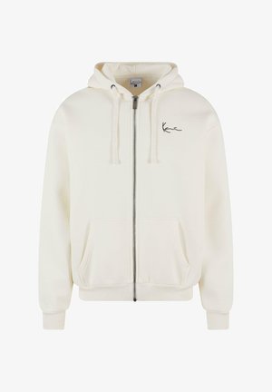 Lynlås hoodie i blødt, kremfarvet stof med en sort logo-detalje på brystet. Har en hætte med snøre og to frontlommer.