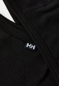 Svart stoff nærbilde som viser en glatt tekstur og fin søm, med en hvit "HH" etikett på sort bakgrunn.