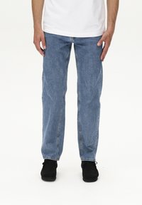 Jeans in denim blu chiaro con taglio dritto, dotati di tasche frontali, cuciture visibili e vita classica, abbinati a scarpe nere.