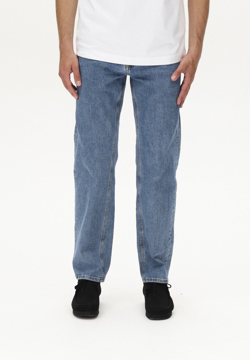Jeans in denim blu chiaro con taglio dritto, dotati di tasche frontali, cuciture visibili e vita classica, abbinati a scarpe nere.