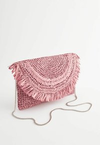 Pochette tissée rose avec rabat à franges et bandoulière chaîne argentée sur fond blanc.
