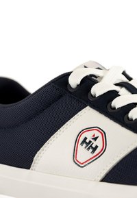 Sneaker blu navy con dettagli in pelle bianca, parte superiore in mesh testurizzato e lacci bianchi. Presenta un badge logo rosso e blu sul lato.