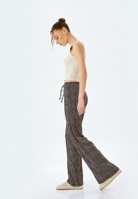 Geweven, high-waisted broek in bruin en zwarte strepen, met een elastische tailleband, gecombineerd met een lichte tanktop en zachte slippers.