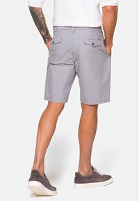 Męskie szare i białe szorty w kratkę, do kolan, z dwiema tylnymi kieszeniami, wykonane z lekkiego materiału, w zestawieniu z szarymi zamszowymi sneakersami.