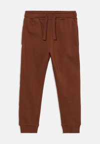 Bruine katoenen joggers met een elastische tailleband, trekkoord, zijzakken en cuffs op de enkels, plat gelegd op een witte achtergrond.