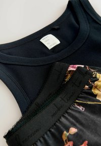 Svart blommönstrad cami-top lagd över en marinblå tank. Tanktoppen har ribbad textur, medan cami-toppen har spetsdetaljer och elastiska inslag.