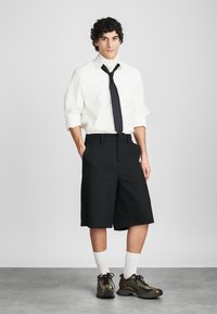 Biele košele s dlhým rukávom a zvinutými manžetami, čierna kravata a čierne šortky do kolien. Nosí sa s teniskami s camo vzorom a bielymi ponožkami.