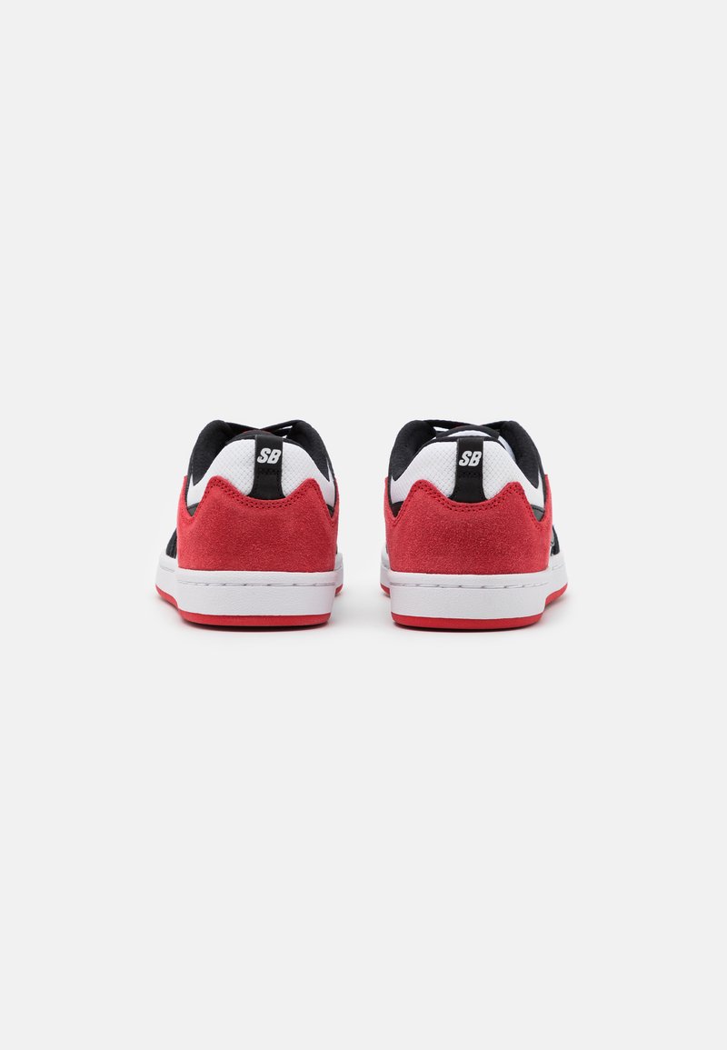 Czerwono-czarne sneakersy z białymi akcentami, posiadające zamszową cholewkę, wyściełany kołnierz i gumową podeszwę. Logo "SB" na pięcie.