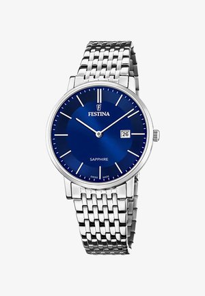 Srebrny zegarek ze stali nierdzewnej z niebieską tarczą, białymi znacznikami godzinowymi i wyświetlaczem daty. Posiada bransoletę z metalowych ogniw oraz szkiełko szafirowe.