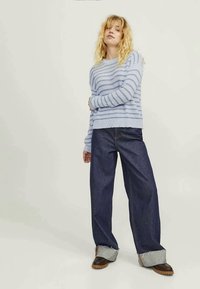 Világoskék csíkos pulóver, puha anyagból készült, magas derekú sötétkék farmer széles szárú nadrággal párosítva. Finoman feltekert ujjak az alján.