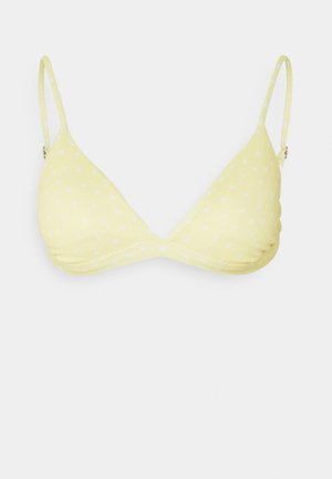 Dzeltena bikinija augšdaļa ar teksturētu audumu, trīsstūra formas bļodiņām un baltām punktiņām. Iespējamas regulējamas siksnas un sānu krokas, lai nodrošinātu labu piegādi.