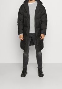 Czarna puchowa kurtka z kapturem, z pikowanym wzorem, zamkiem błyskawicznym z przodu i głębokimi bocznymi kieszeniami. Nosi się ją na szarej koszuli i czarnych dżinsach.