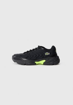 Schwarzer Sneaker mit wellenförmigem Mesh-Design, Schnürverschluss, neon-grüner Sohlendetail und kleinem grünem Krokodil-Logo an der Seite.