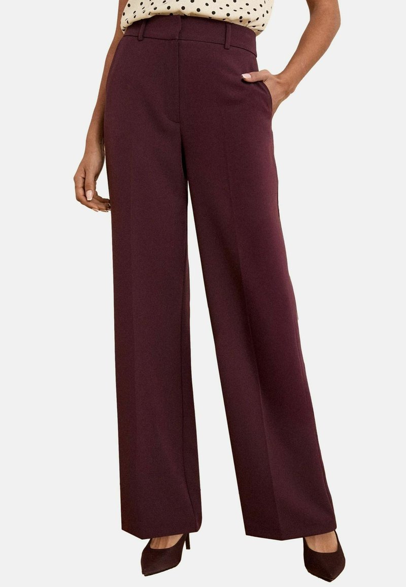 Pantalons larges bordeaux avec une coupe ajustée, dotés de poches latérales et d'une texture lisse. Portés avec un haut à pois et des chaussures à talons.