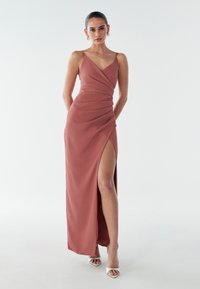 Rozā satīna kleita ar drapējuma dizainu, tai ir augsts šķēlums un plānas lencītes. Gluda tekstūra un eleganta silueta. Kvadrātveida baltas augstpapēžu kurpes.