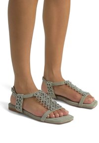 Sandalias grises con acentos decorativos de cuentas plateadas, diseño de punta abierta y tira en el tobillo. Suela plana con textura mínima y una silueta elegante.