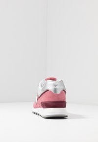 Růžové a bílé tenisky New Balance zobrazené ze zadní strany, umístěné na bílé ploše s jednoduchým bílým pozadím.