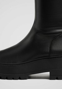 Czarne botki za kostkę z gładką skórzaną cholewką, masywną gumową podeszwą i teksturowanym detalem z boku. Głęboki wzór bieżnika na podeszwie.