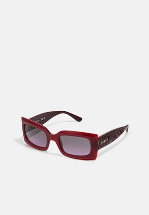 Occhiali da sole rettangolari rossi con lenti sfumate. Montatura spessa e lucida e aste in un profondo rosso scuro finemente decorate con un design floreale.