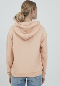 Felpa color pesca con cappuccio spazioso, polsini a costine e vestibilità comoda. Il tessuto appare morbido con una superficie liscia e cuciture minime.