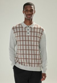 Lys grå langærmet polo sweater med et brunt og burgundy ternet mønster, med krave og tre-knap lukning. Blød tekstur.