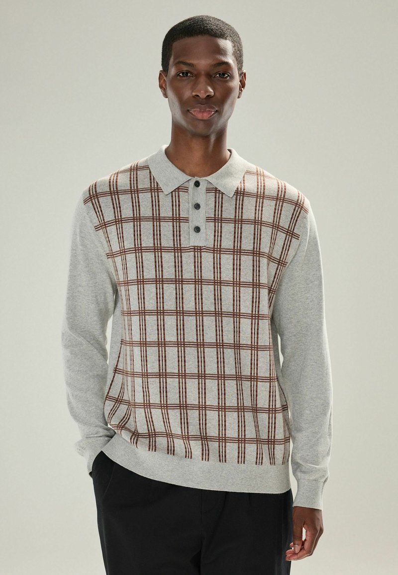 Lys grå langærmet polo sweater med et brunt og burgundy ternet mønster, med krave og tre-knap lukning. Blød tekstur.